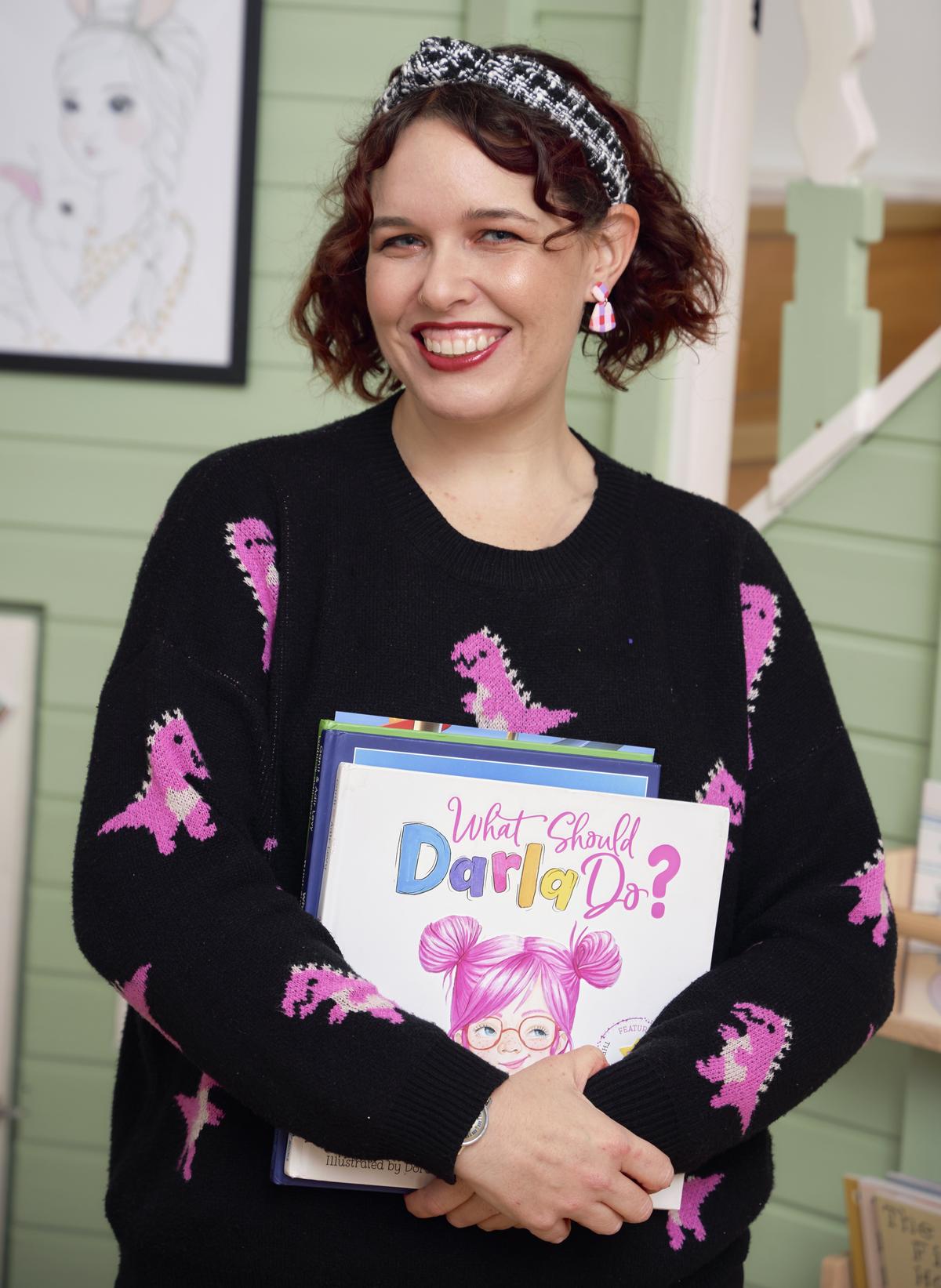 Emily Pye smiling, holding a stack of children's books