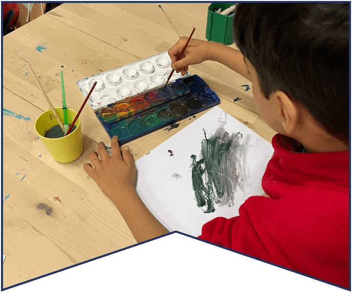 A child painting at a wooden table with watercolor supplies